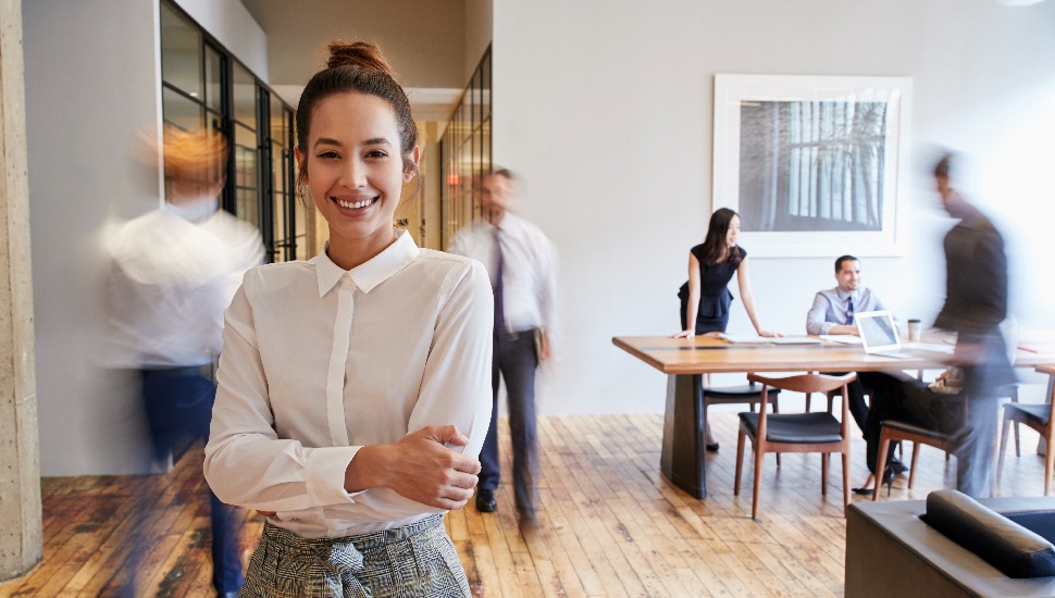 A female professional in an office with other people walking in the background