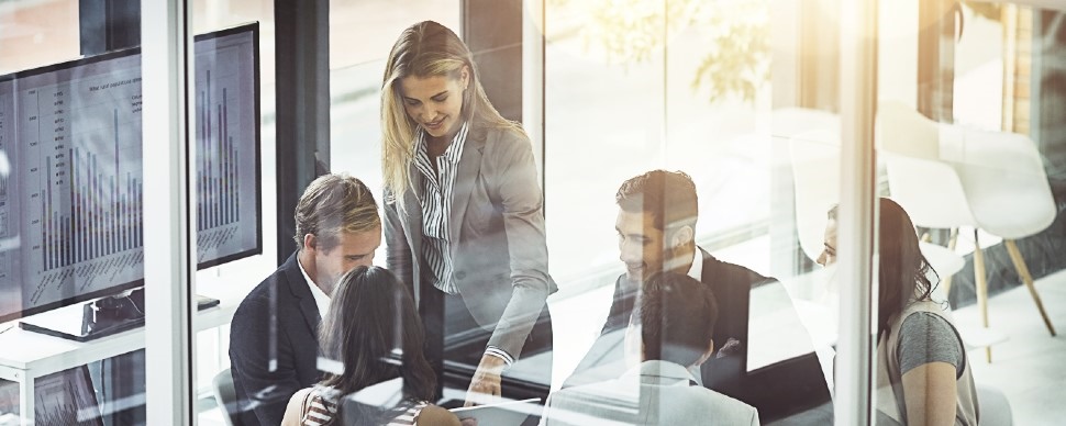 6 white-collar professionals sitting at one table and looking at something on a computer screen, while smiling