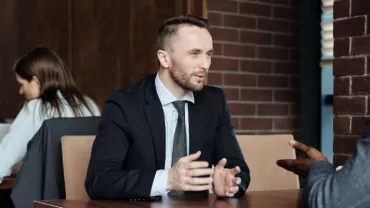 Two men in suits having a discussion at a table in a coffee shop.