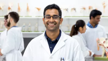 Smiling student in a lab coat in a classroom with anatomical models.