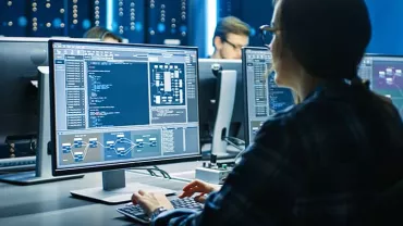 Person working at a computer with code on the screen in a tech office.