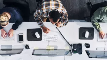 Top view of three people working at computers in an office setting.