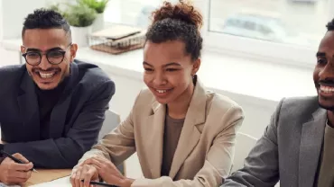 Three people sitting at a desk, smiling during a meeting.