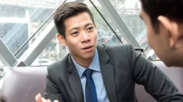 Two businessmen discussing in a modern office with large windows.