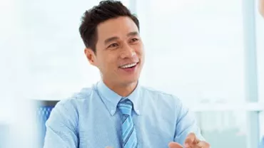 Smiling man in a blue shirt talking to a colleague in an office.