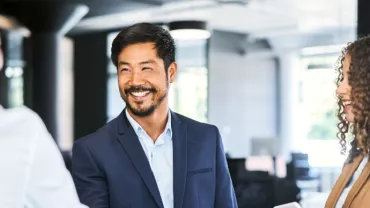 Smiling businessman shakes hands with a colleague in a bright office.