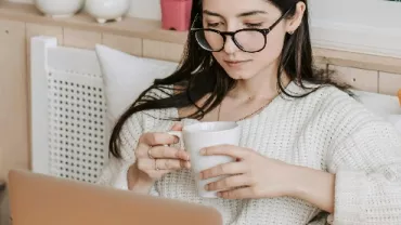 A woman holding a mug while looking at her computer screen