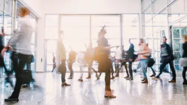 People walking through a busy glass building entrance.