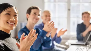 A group of office workers of different ethnicities and in casual wear, chatting and laughing on the same table