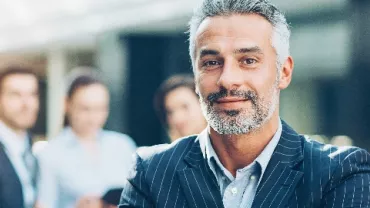 Confident man in a suit with a group of colleagues in the background.