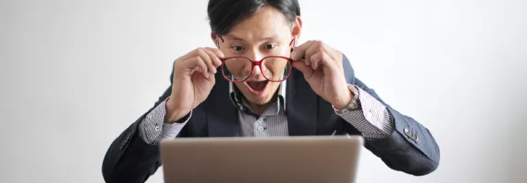 Surprised man with glasses looks at laptop