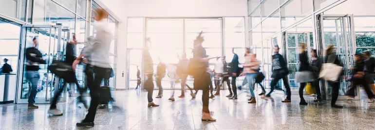 People walking through a busy glass building entrance.