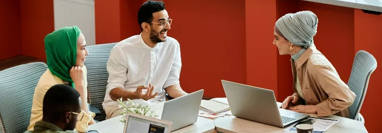 Group of professionals discussing at a table with laptops.